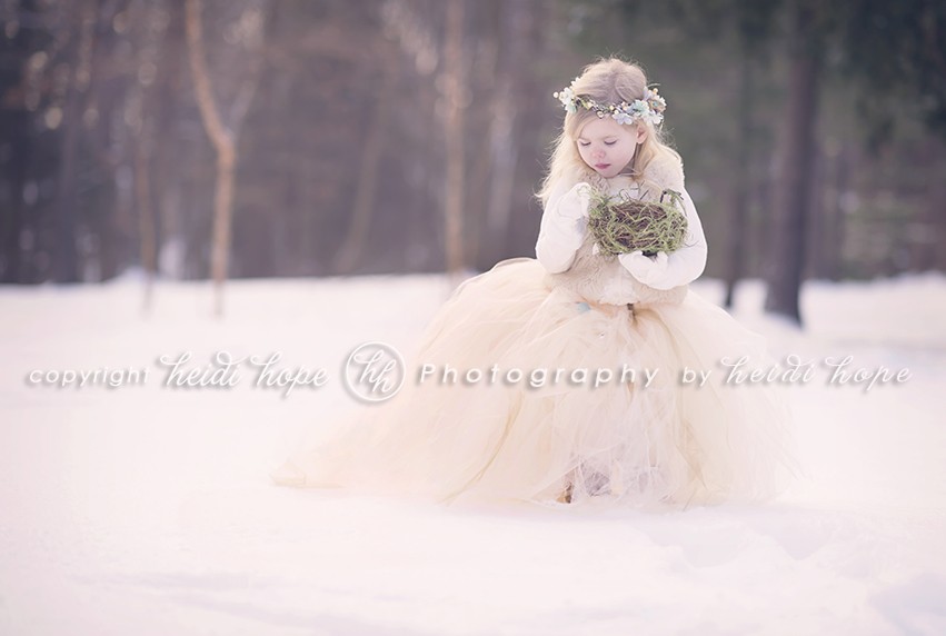 Girl in snowy woods in large tutu holding nest
