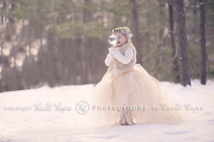 Girl in snow with tutu playing with a magnifying glass